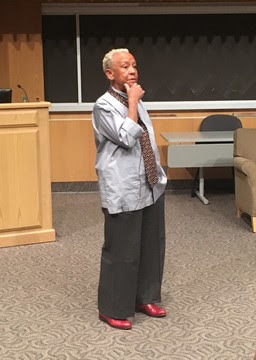 Nikki Giovanni looking contemplative at the front of an auditorium.